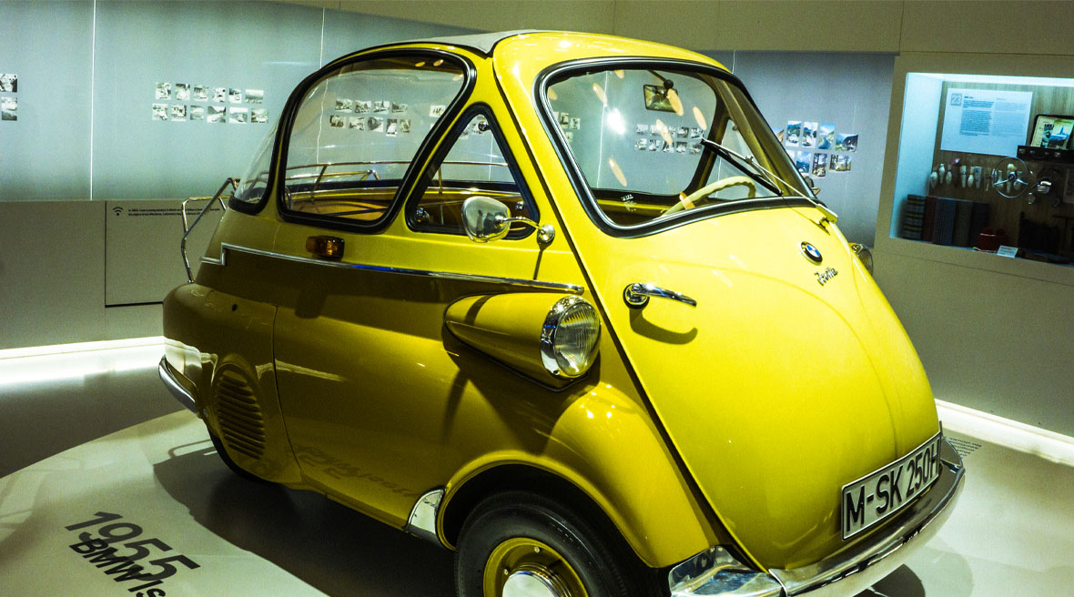 A very small retro 3-seater yellow car on display in a museum